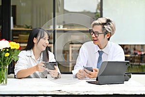 Laughing business colleagues sitting in front of office buildings and discussing about their work