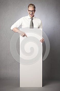 Laughing businessman pointing finger at white blank poster.