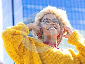 Laughing carefree African American woman with afro hair listening to music with headphones in a city