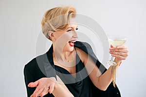 Laughing Caucasian mature stylish elegant woman in tuxedo with glass of sparkling wine.