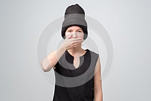 Laughing caucasian woman in black hat covers mouth with hand
