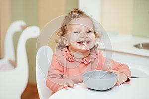 Laughing and cheerful baby girl eats pasta in the kitchen