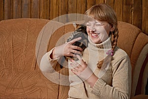 Laughing cheerful woman in a knitted sweater holds a tabby kitten on her shoulder. Indoors with copy space