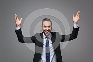 Laughing cheerful young business man in classic black suit shirt tie posing isolated on grey wall background