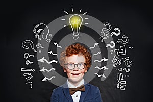 Laughing child boy with lightbulb and question marks on blackboard background