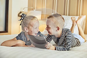 Laughing children lying on their bed using a tablet