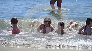 Laughing children are lying on their stomachs in splashing sea waves on a beach