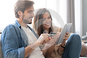 Laughing couple sitting on the couch shopping online with tablet pc at home in the living room.