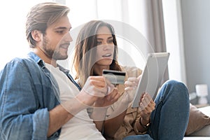 Laughing couple sitting on the couch shopping online with tablet pc at home in the living room.