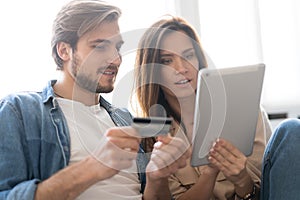 Laughing couple sitting on the couch shopping online with tablet pc at home in the living room.