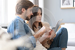 Laughing couple sitting on the couch shopping online with tablet pc at home in the living room.