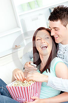 Laughing couple on sofa with popcorn and remote