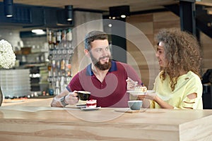 Laughing couple of young students drinking coffee, eating cakes in cafe.