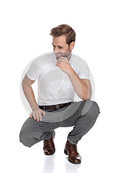 Laughing crouched smart casual man thinks and looks to side