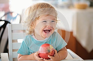 Laughing cute child eating apple. Cute baby eat apples. Portrait of cute smiling laughing Caucasian child kid sitting in