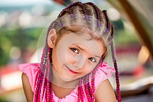 Laughing cute girl portrait. Cute small girl smiling. Sweet child girl with pink-red afro-pigtails dreadlocks. Child in