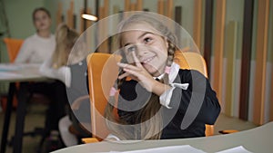 Laughing cute schoolgirl smiling and talking. Portrait of pretty Caucasian girl sitting at desk in classroom in public