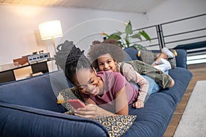 Laughing darkskinned woman and little daughter lying on sofa