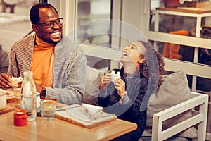 Curly dark-haired daughter laughing while having lunch with father