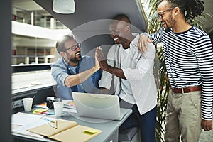 Laughing designers high fiving together in an office meeting pod