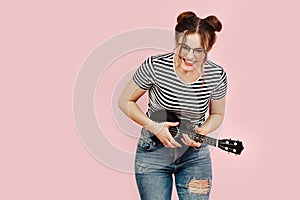 Laughing eccentric lady in striped shirt holding ukulele. Over pink background