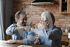 Laughing elderly father millennial son bump fists after finishing boardgame