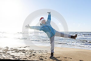 Laughing elderly woman in Santa Claus hat on the seashore in winter. Active lifestyle during the holidays.Happy New Year. Full