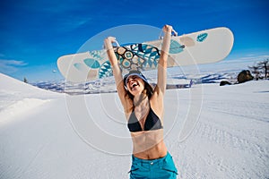 Laughing emotional young woman in a swimsuit and hat holding a snowboard in her hands in winter. Extreme. Euphoria. Cheerful
