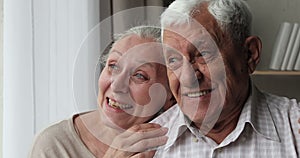 Laughing faces of aged spouses cuddling talking looking at distance
