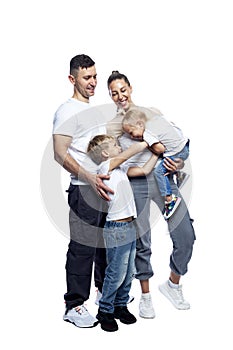 Laughing family with children. Dad, mom, little son and daughter in white t-shirts and jeans happily hug. Love and tenderness.
