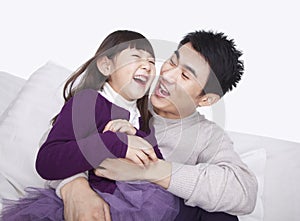 Laughing father tickling daughter and bonding on the sofa, studio shot