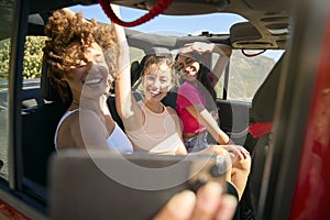 Laughing Female Friends Having Fun Posing For Selfie In Open Top Car On Road Trip