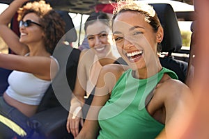 Laughing Female Friends Having Fun Posing For Selfie In Open Top Car On Road Trip