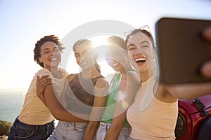 Laughing Female Friends On Vacation Having Fun Posing For Selfie By Open Top Car On Road Trip