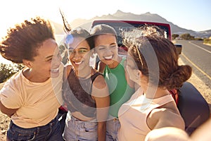 Laughing Female Friends On Vacation Having Fun Posing For Selfie By Open Top Car On Road Trip