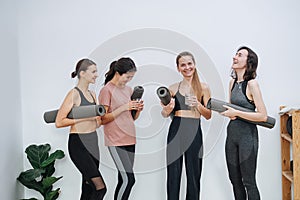 Laughing friendly women socialising at yoga club, holding rolled mats under arm