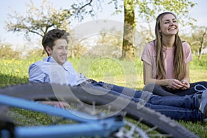 Laughing friends spending time on a meadow with trees on a sunny day, in the foreground the wheel of a bicycle