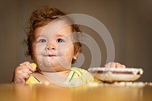 Laughing funny baby with dirty food face. Happy child spoon eats itself.