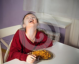 Laughing funny kid girl eating tasty spaghetti on the dinner on the home kitchen. Closeup