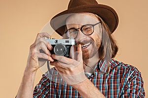 Laughing ginger man wearing eyeglasses and hat using retro camera