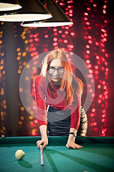 Laughing ginger woman playing billiard holding a cue