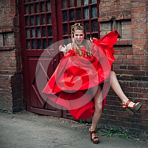 laughing girl with beautiful make-up, in a long red dress, jumps along the street