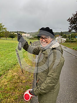 Laughing girl holding feces bag of dog in hand at rainy autumn day