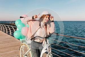 Laughing girl in pink cap coming to sea after bike trip to enjoy beautiful view in morning. Adorable brunette young