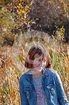 A laughing girl with red hair is standing under the falling fluff.