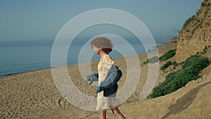 Laughing girl running down seashore with arms outstretched. Woman walking beach.
