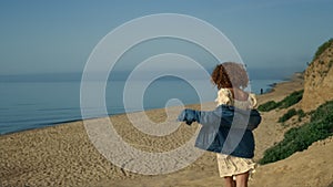 Laughing girl running down seashore with arms outstretched. Woman walking beach.