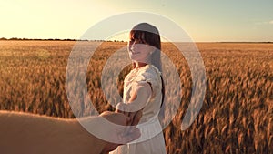 Laughing girl runs across the field with wheat holding a man`s hand in the glare of the golden sun. Slow motion.