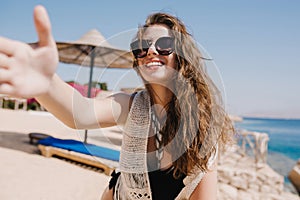 Laughing girl in stylish sunglasses with light-brown hair making selfie on sea resort having fun on beach. Portrait of