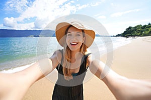 Laughing girl takes self portrait on empty tropical island in her summer vacation. Selfie of smiling tourist woman on Ilhabela